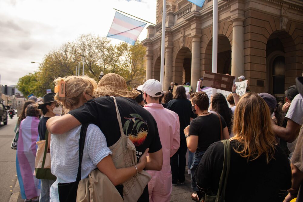Two protestors embrace amid a crowd gathered outside Hobart City Hall.